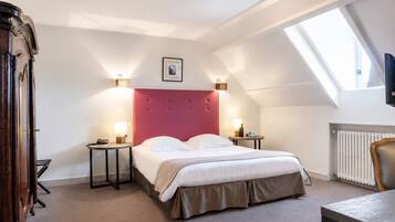 A bedroom with a bed, bedside tables, a dresser, a radiator, and a skylight.