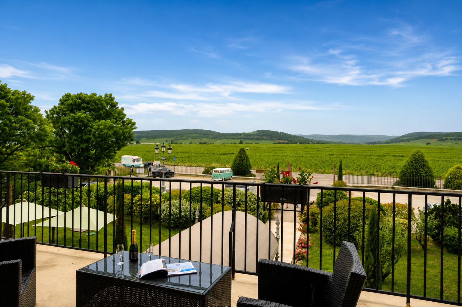 A balcony with outdoor furniture, a view of a green landscape, and a road with vehicles.