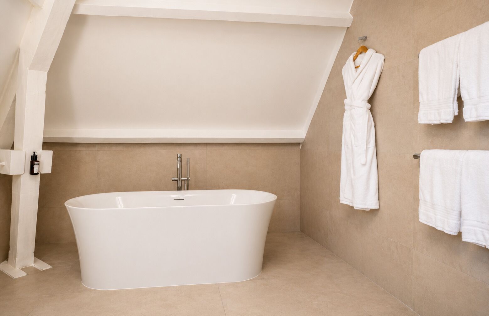 Une salle de bain moderne avec une baignoire sur pieds, un porte-serviettes avec plusieurs serviettes et un flacon de shampoing fixé au mur.