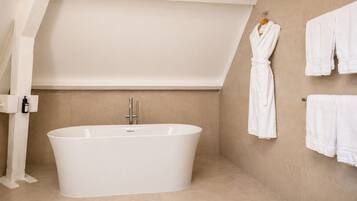 Une salle de bain moderne avec une baignoire sur pieds, un porte-serviettes avec plusieurs serviettes et un flacon de shampoing fixé au mur.
