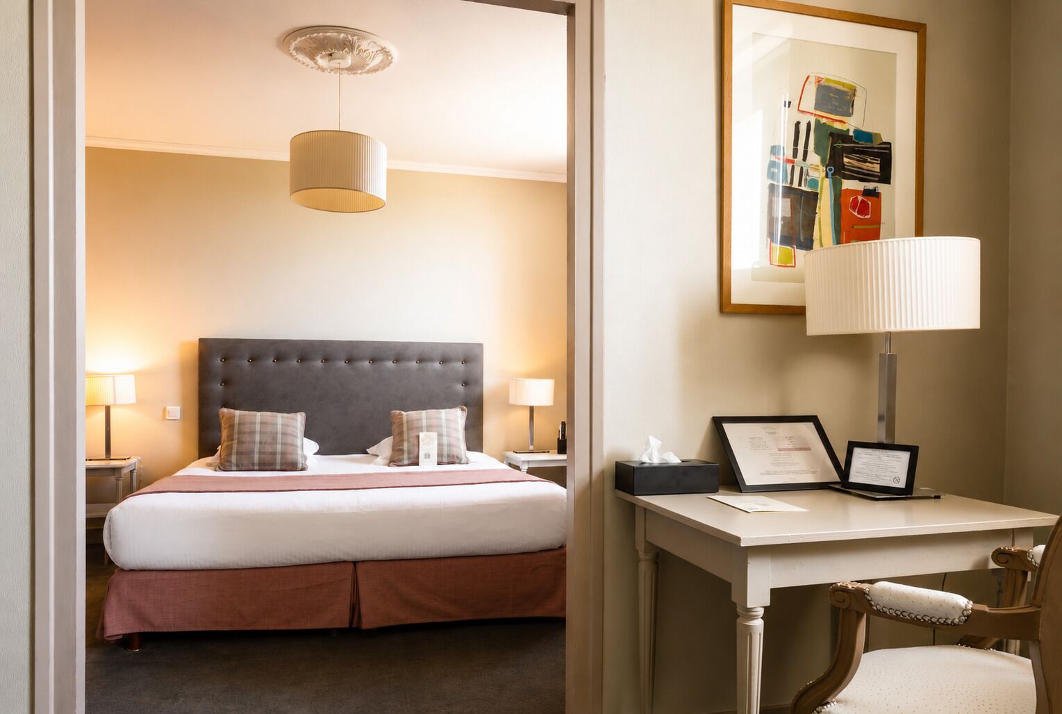 Habitación de hotel con cama, lámparas de noche, escritorio con silla y un cuadro en la pared.