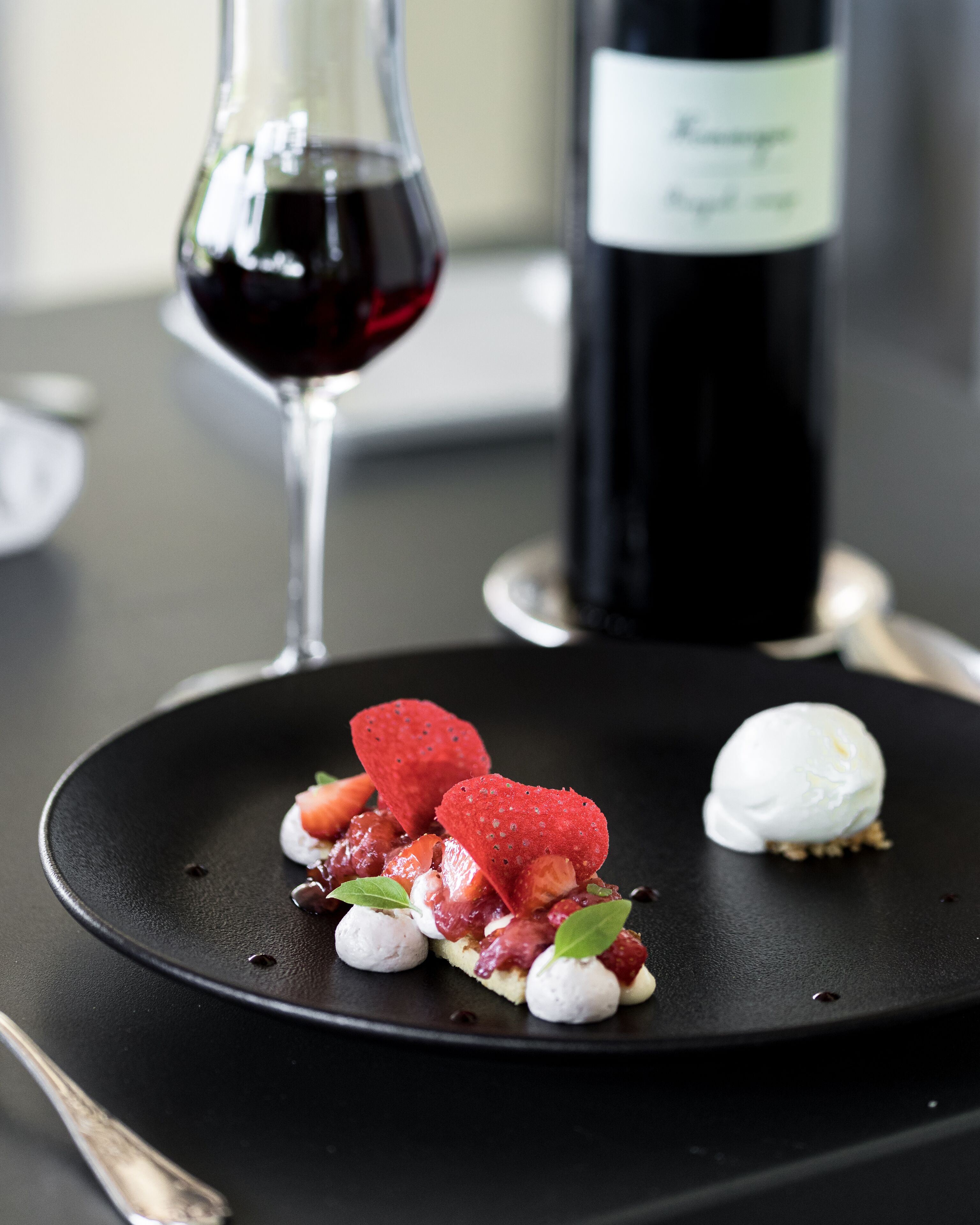 A dessert plate with strawberries, a scoop of ice cream, and a bottle of wine in the background.