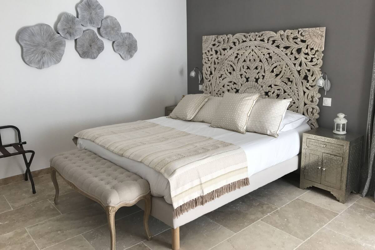 A bedroom with a large bed, a bench, a decorative headboard, and a wall art piece.