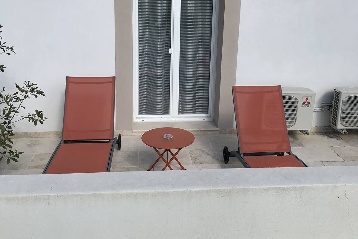 A balcony with two red lounge chairs, a small round table, and a window with frosted glass.