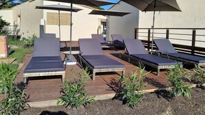 En solterrass med solstolar och parasoller, ett trädäck och en byggnad i bakgrunden.