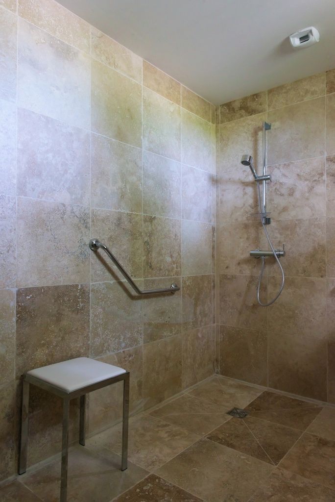 Zona de ducha con barra de apoyo, ducha y un taburete pequeño.