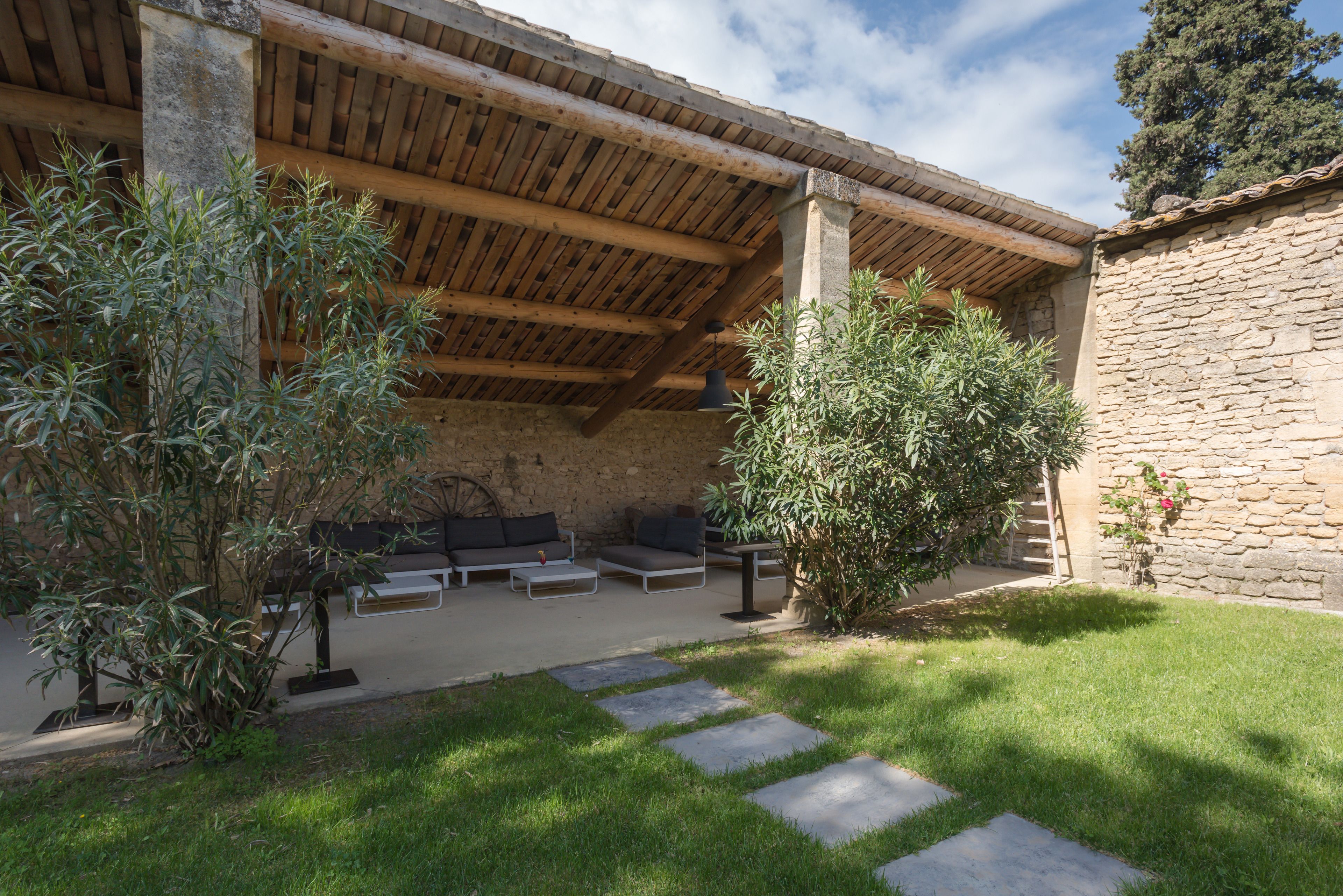 Un área de estar al aire libre cubierta, con paredes de piedra, techo de madera y césped.