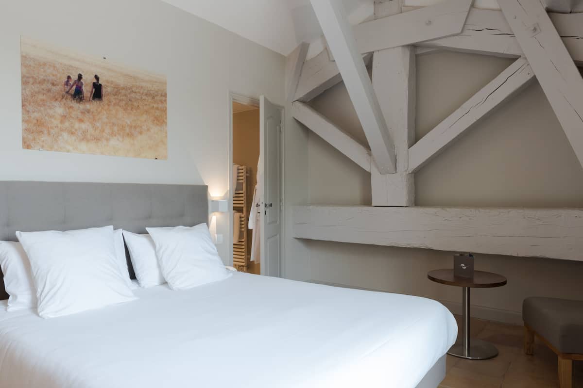 A bedroom with a large bed, a small round table, and a painting on the wall.