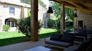 An outdoor patio with stone columns, a stone building in the background, and a seating area with cushions.