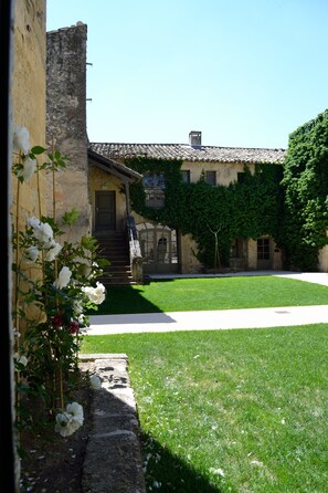 A courtyard with a stone building, a grassy lawn, and a white flower bush. - La Bégude Saint-Pierre (Vers-Pont-du-Gard)