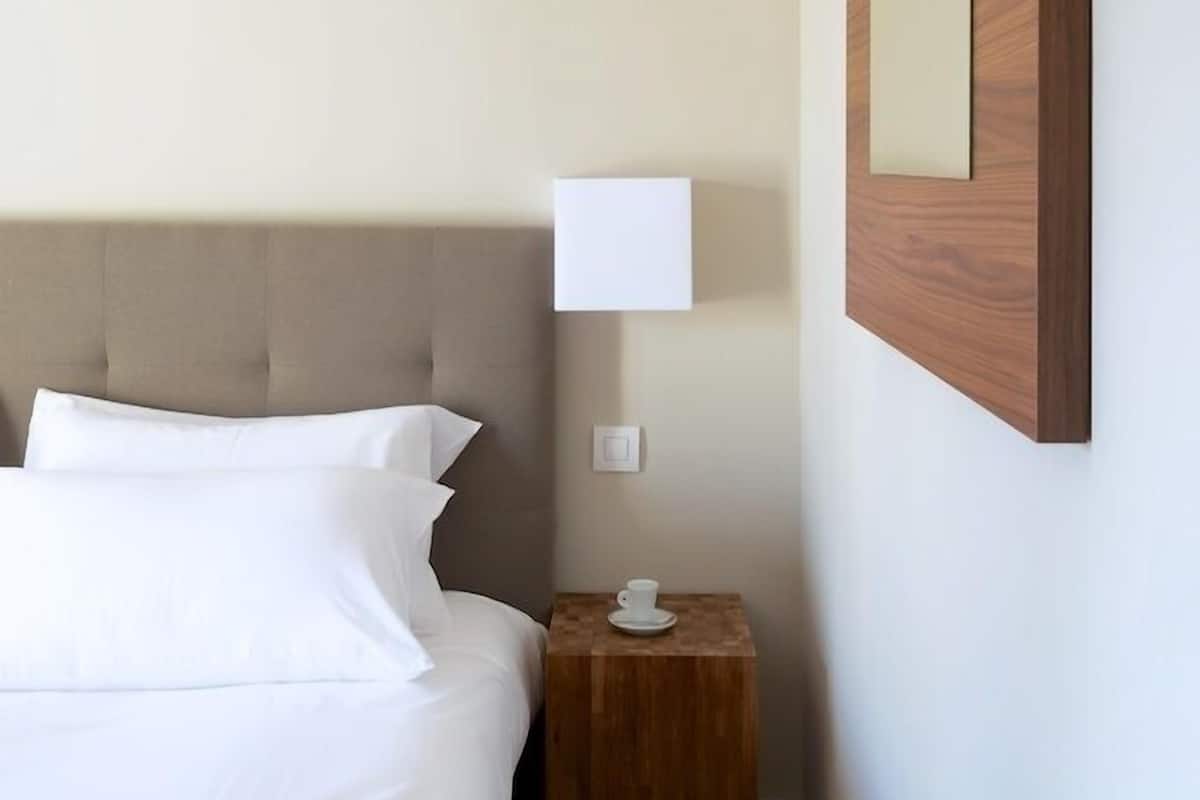 A hotel room with a bed, a bedside table with a lamp, and a wooden panel on the wall.