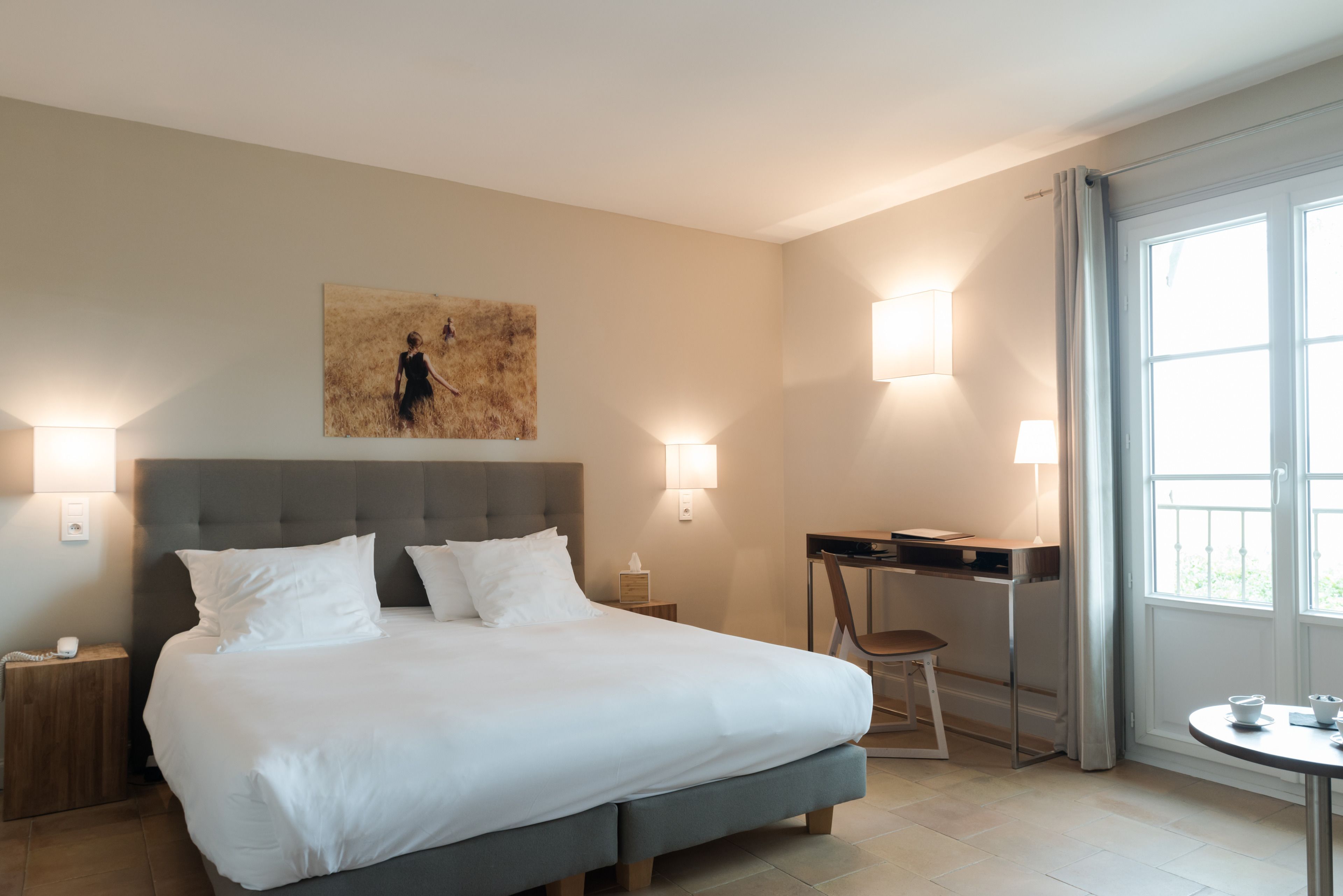 A hotel room with a large bed, bedside tables, a desk, a chair, and a window with curtains.