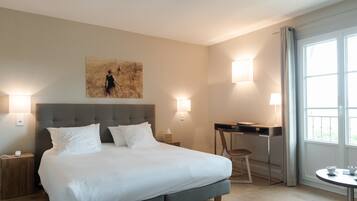 A hotel room with a large bed, bedside tables, a desk, a chair, and a window with curtains.
