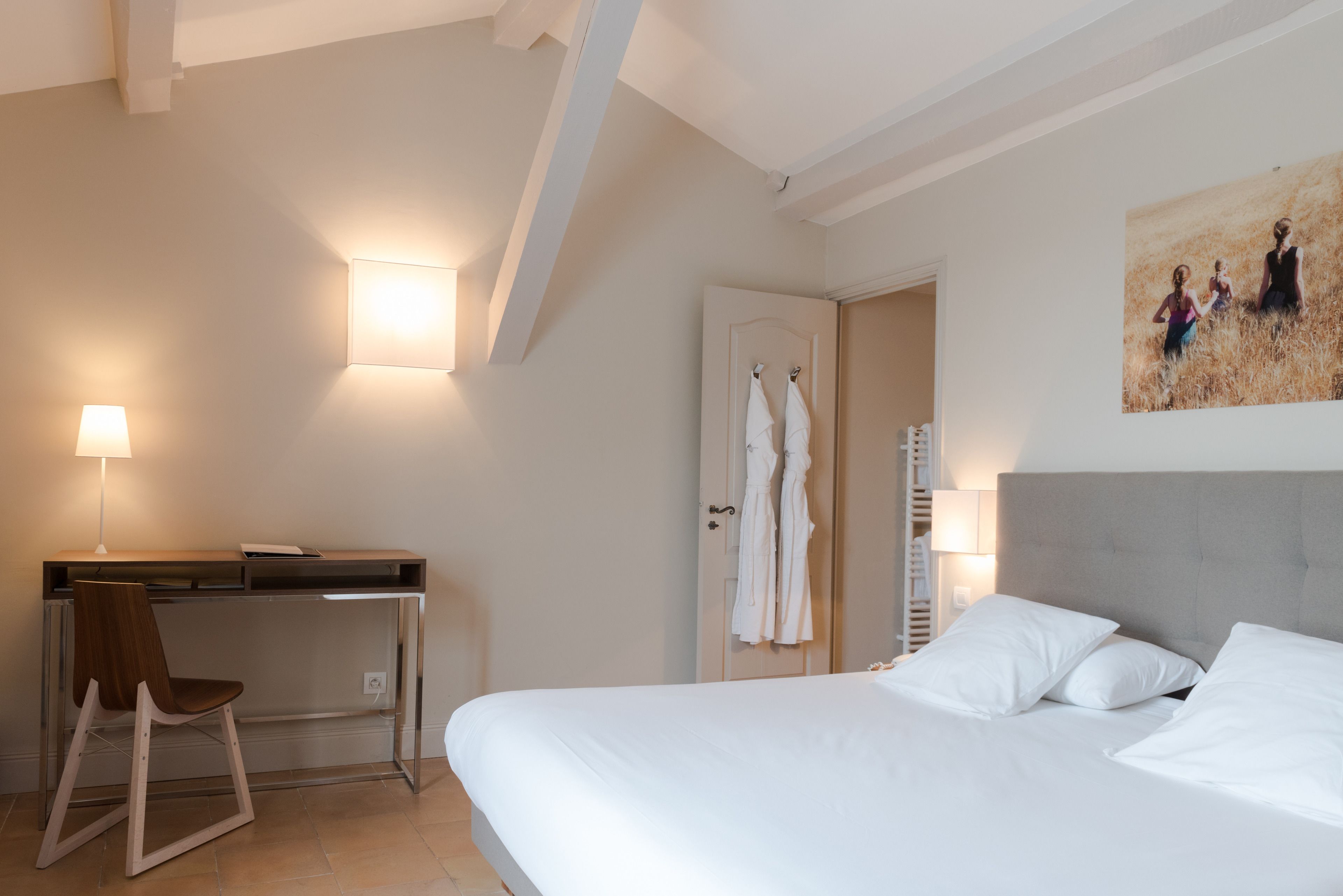 A hotel room with a bed, desk, chair, and a painting on the wall.