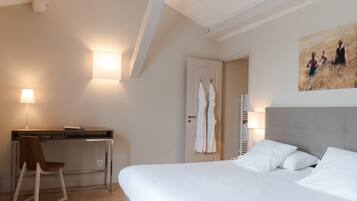 A hotel room with a bed, desk, chair, and a painting on the wall.