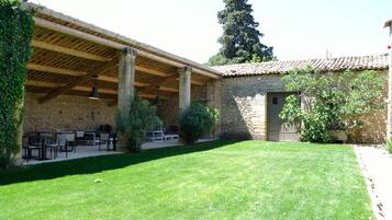 Un bâtiment en pierre doté d’un patio couvert, d’un espace extérieur aménagé pour s’asseoir et d’une pelouse bien entretenue.