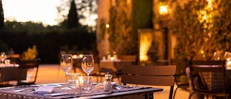 An outdoor dining area with tables set for two, each with wine glasses, a candle, and cutlery.