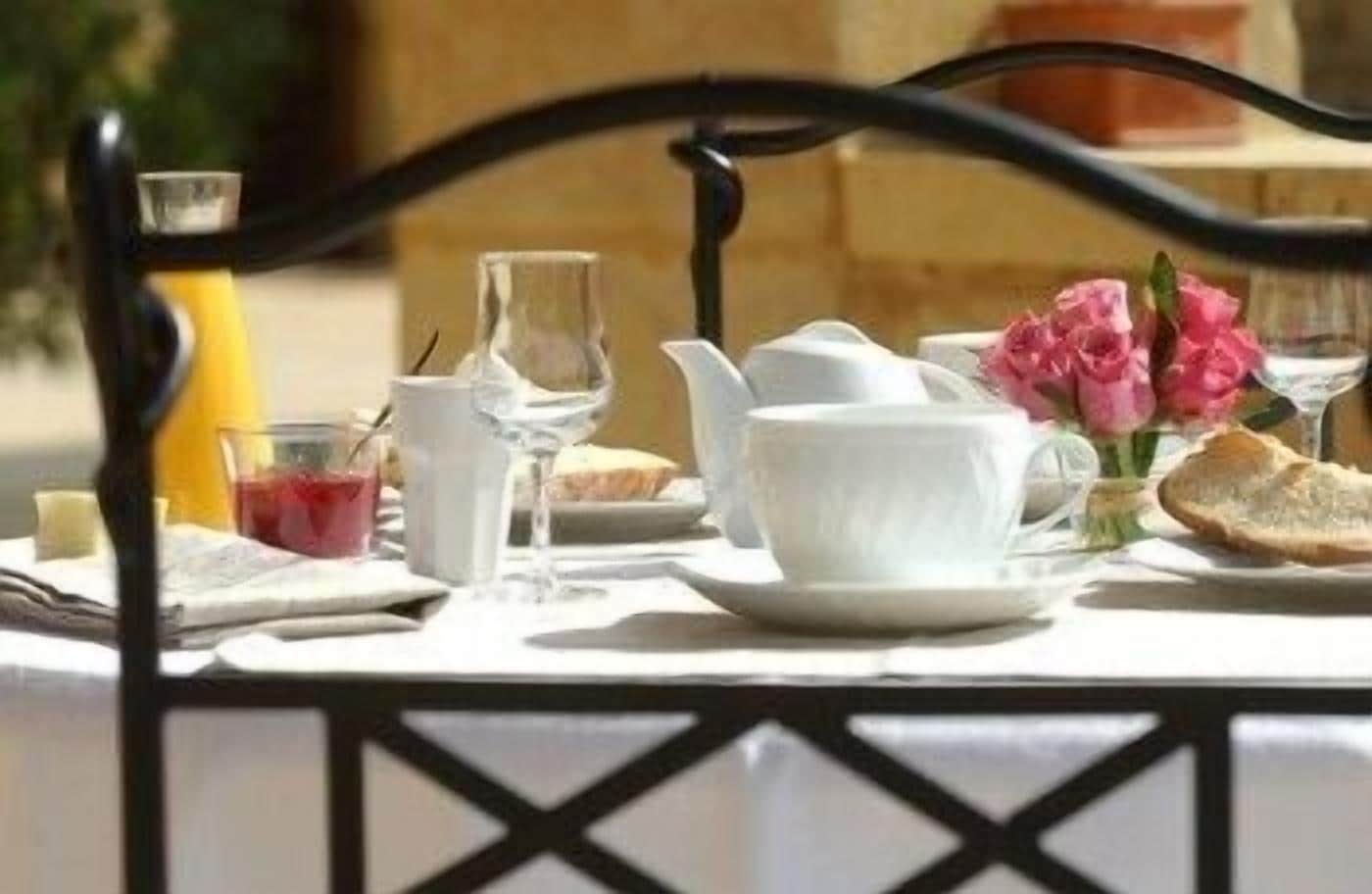 Ett dukat bord för frukost med en kanna, koppar, ett glas juice och en bukett blommor.