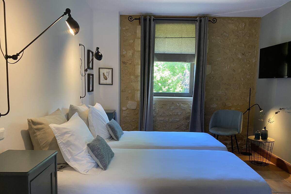 Habitació amb dos llits, escriptori, cadira, televisió i finestra amb cortines.