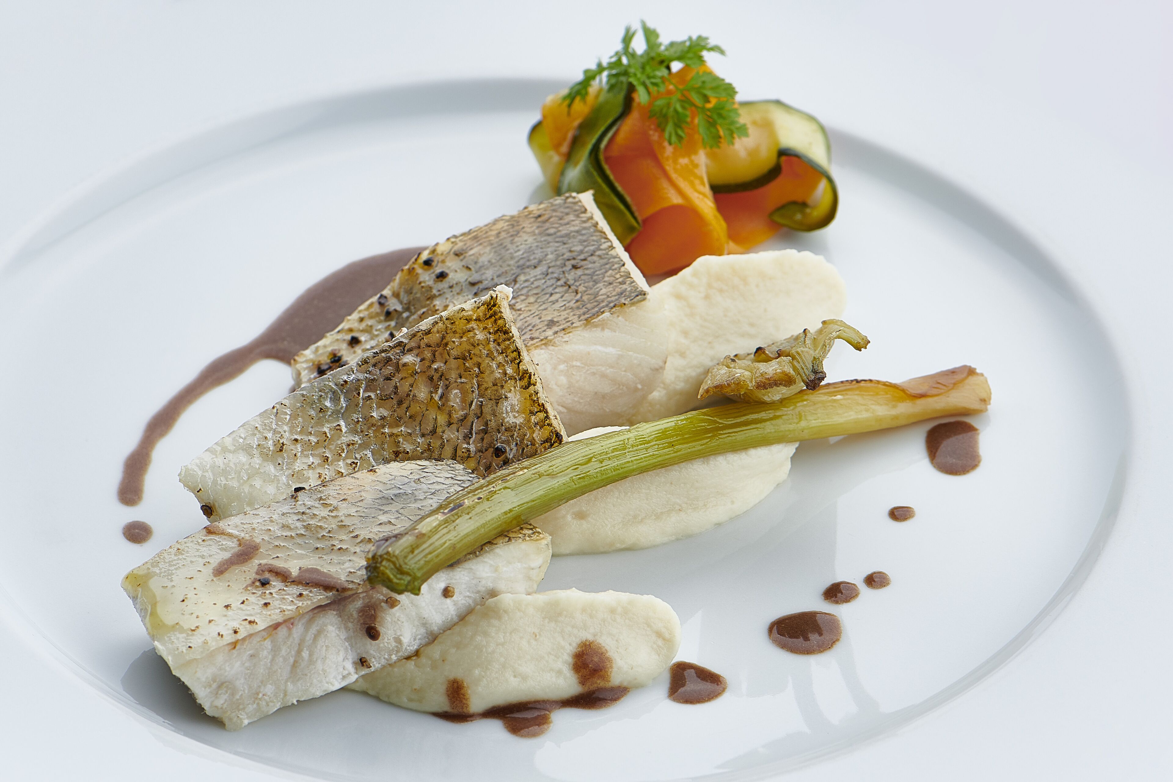 A white plate with a piece of fish, a vegetable, and a garnish.