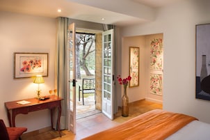 Quarto de hotel com cama, escrivaninha com luminária, cadeira e vista para o exterior.