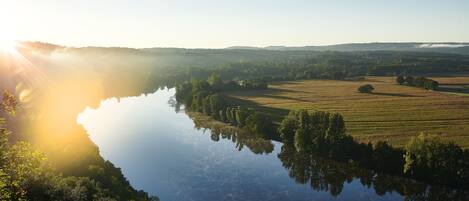A serene landscape with a calm lake reflecting trees and fields, surrounded by hills.