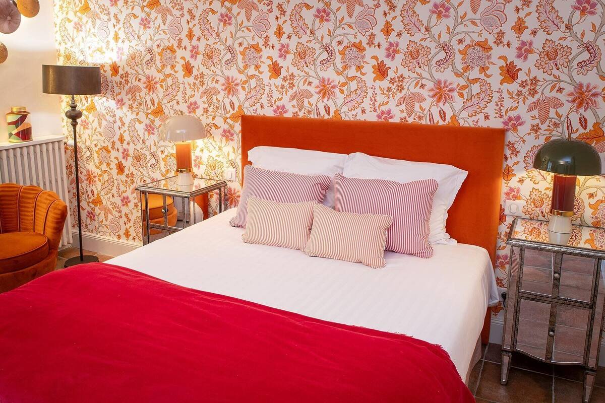 Ein Bett mit roter Decke, gestreiften Kissen und floralem Wandpapier.