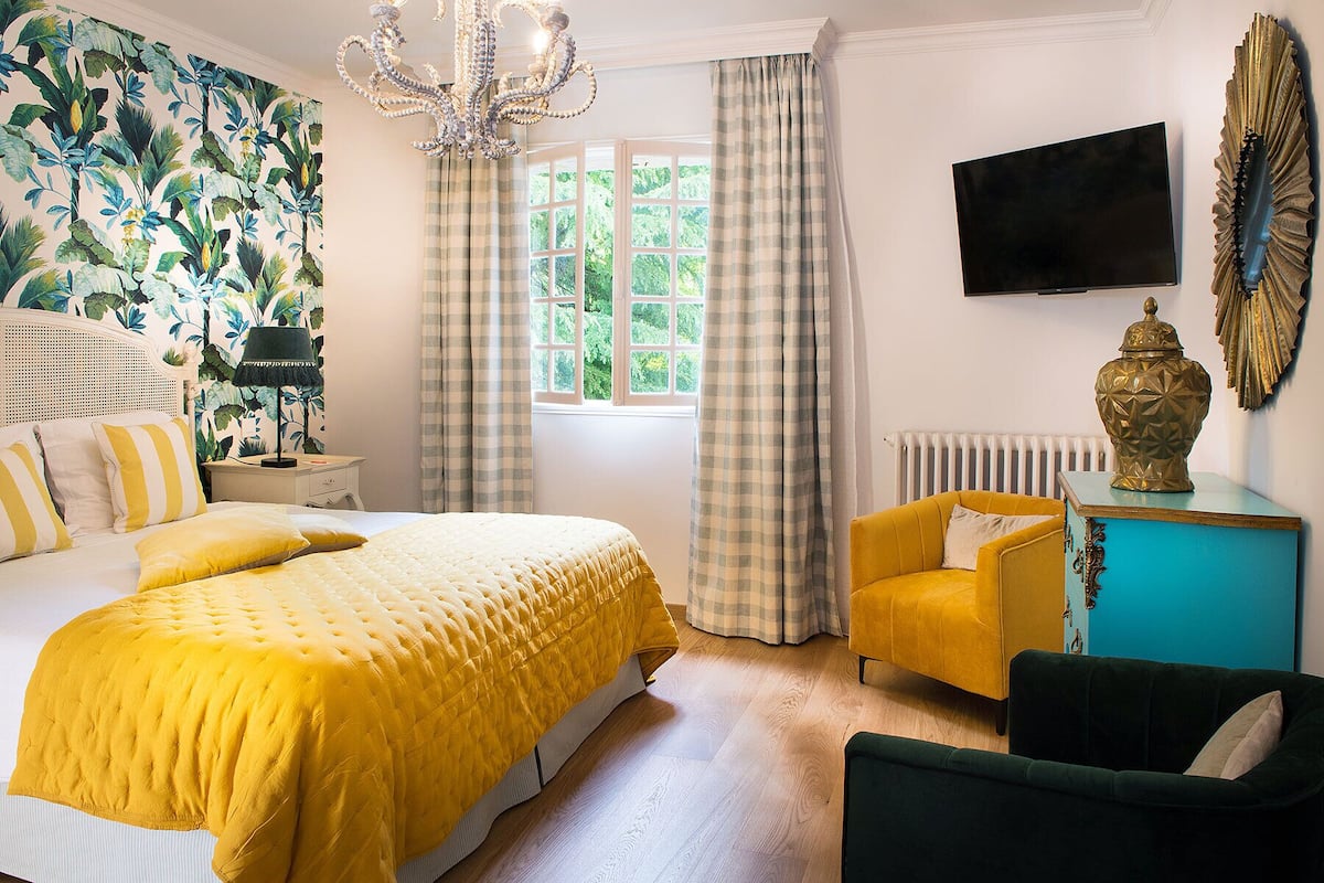 Ein Hotelzimmer mit einem großen Bett, einer Couch, einem Fernseher und einem Fenster mit Vorhängen.