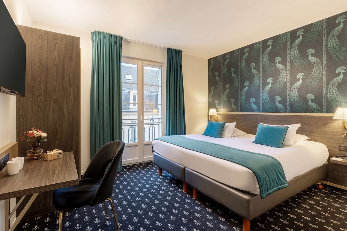 A hotel room with a large bed, a desk with a chair, a TV, and a window with curtains.