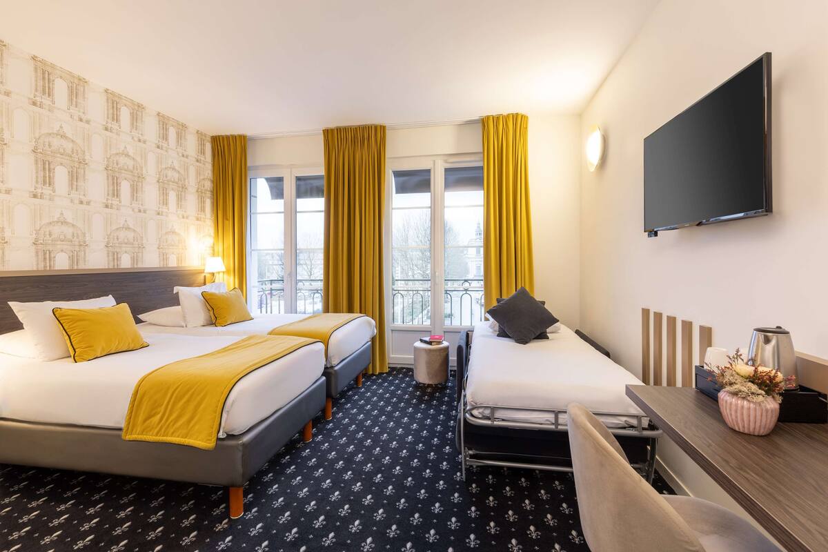 A hotel room with two beds, a desk, a TV, and a window with curtains.