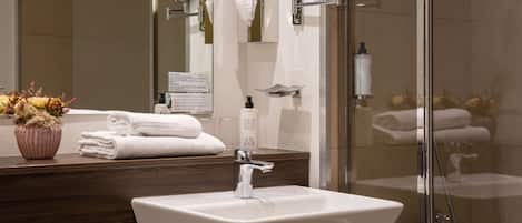 Un baño moderno con lavamanos blanco, cabina de ducha con mampara de vidrio y mueble de tocador de madera con espejo.