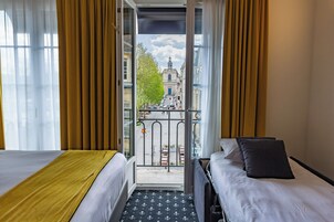 Habitación de hotel con dos camas, un balcón y vista a un edificio con torre.