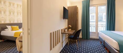 A hotel room with a bed, a desk with a chair, a TV mounted on the wall, and a window with curtains.