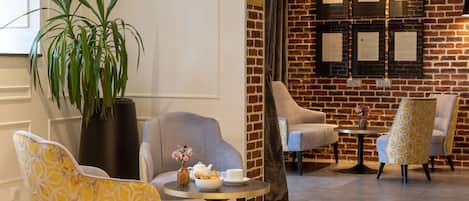 A lobby with a brick wall, a potted plant, and seating arrangements including a round table with a vase and teapot.