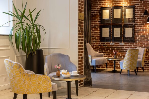 A lobby with a brick wall, a potted plant, and seating arrangements including a round table with a vase and teapot.