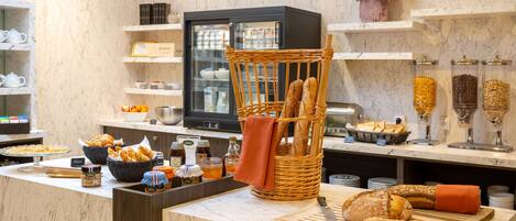 A breakfast buffet with various breads, pastries, and condiments.