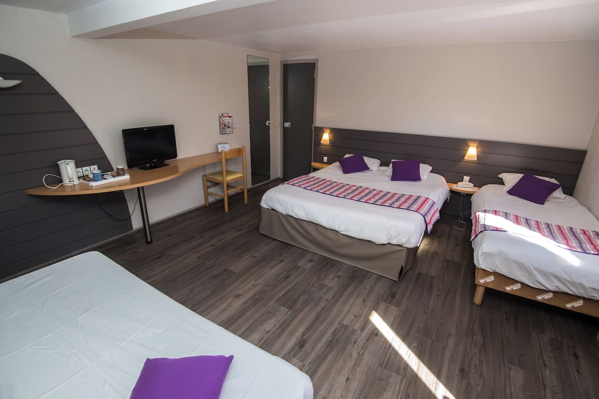 A hotel room with two beds, a desk with a TV, and a chair.