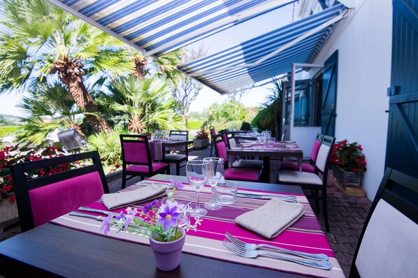 An outdoor dining area with tables set for two, surrounded by chairs and covered by a striped awning. - Kyriad Orthez (Orthez)