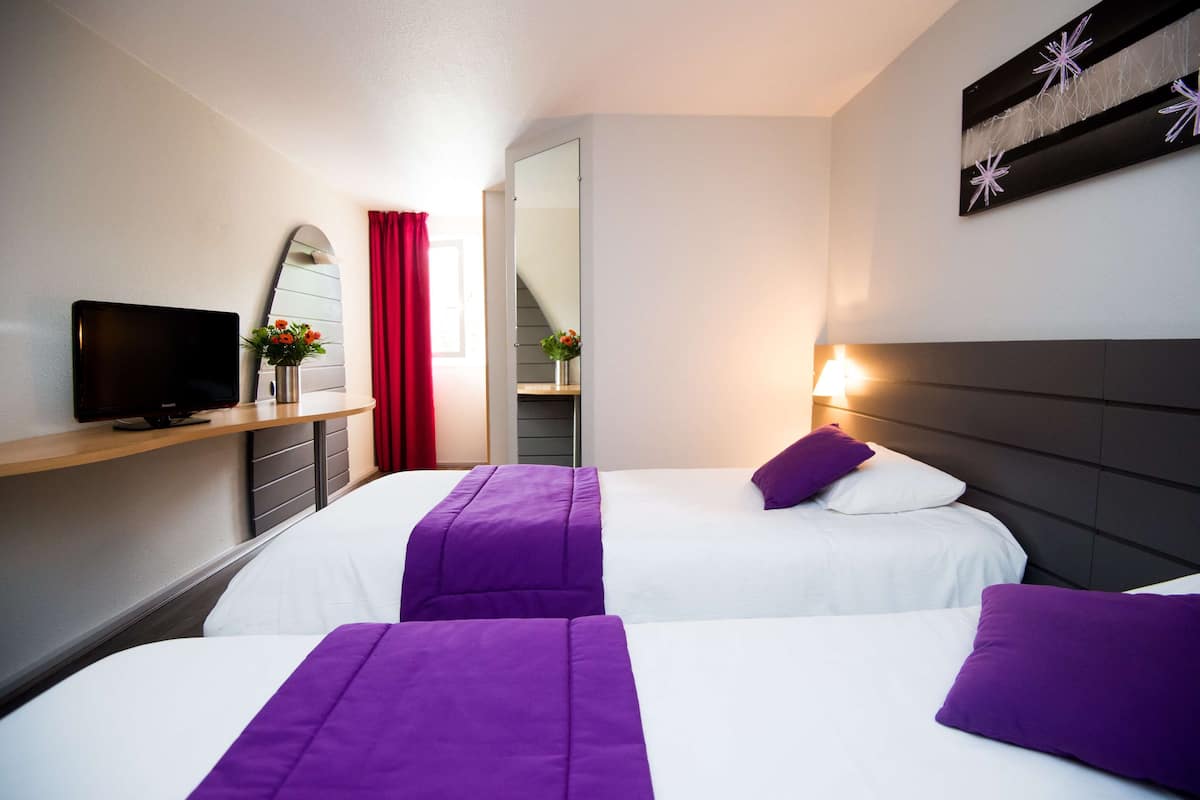A hotel room with two beds, a TV, a mirror, and a red curtain.