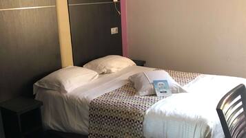 Una cama bien hecha con sábanas blancas y una colcha estampada, una mesita de noche y un cabecero.