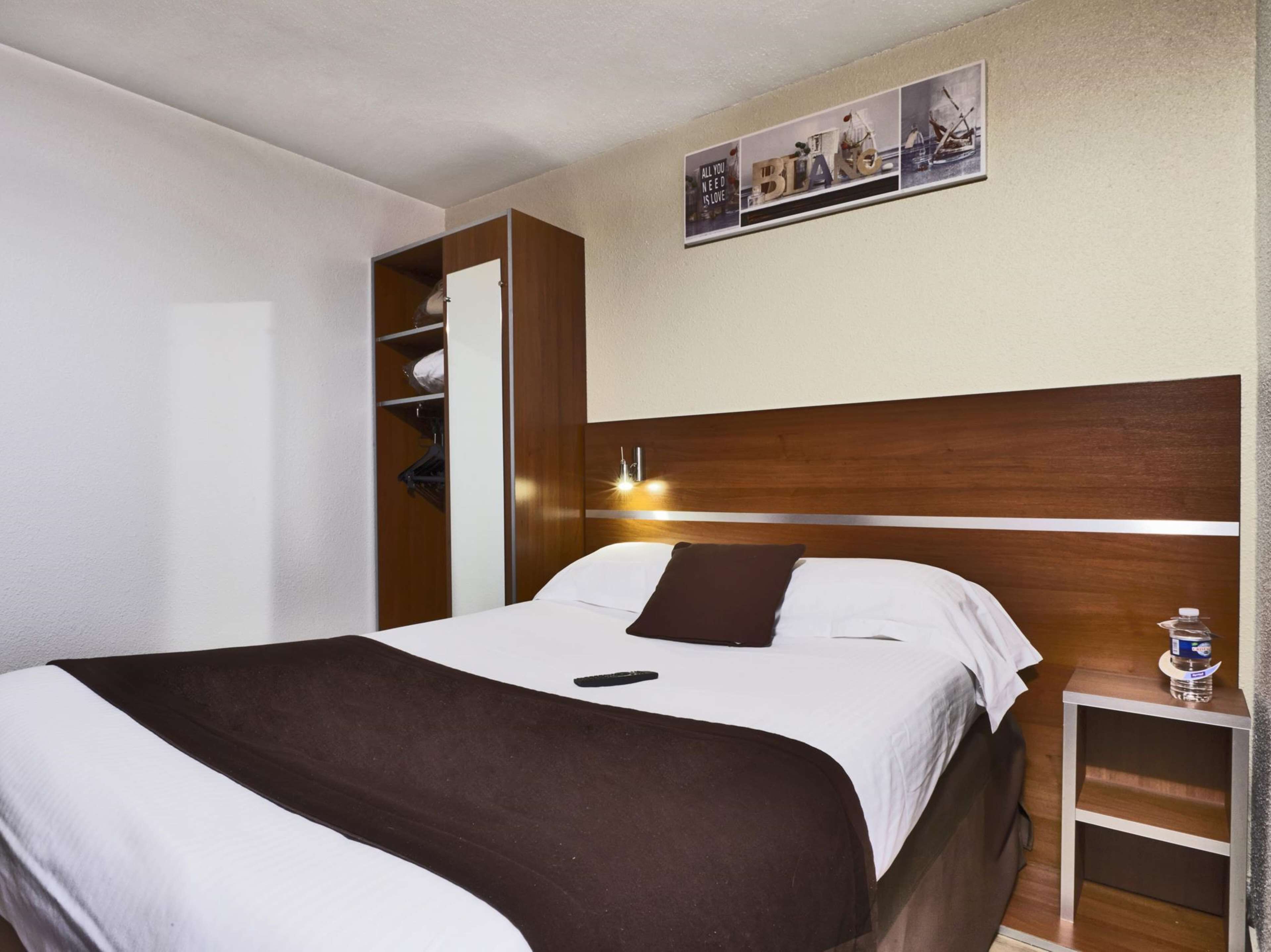 A hotel room with a bed, a nightstand, a wall-mounted shelf, and a framed picture above the bed.