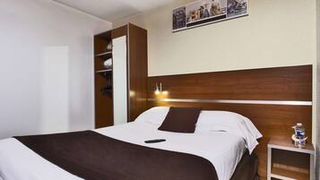 A hotel room with a bed, a nightstand, a wall-mounted shelf, and a framed picture above the bed.