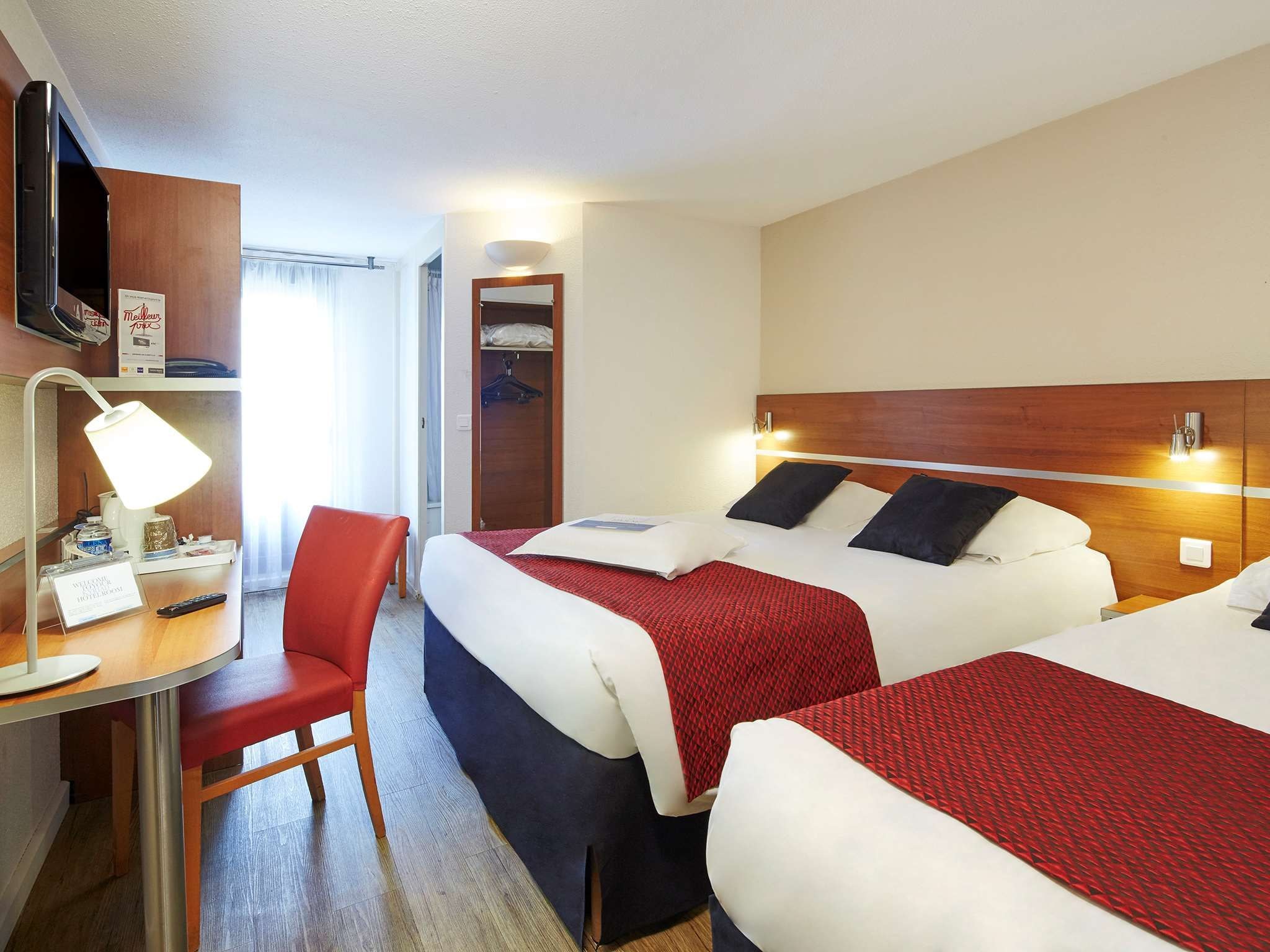 A hotel room with two beds, a desk with a chair, a TV, and a closet.
