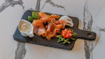 A slate serving board with smoked salmon, cherry tomatoes, and green beans on a marble countertop.