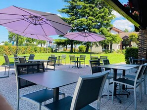 An outdoor patio with tables and chairs, purple umbrellas, and a view of a building and trees. - Kyriad Meaux (Meaux)