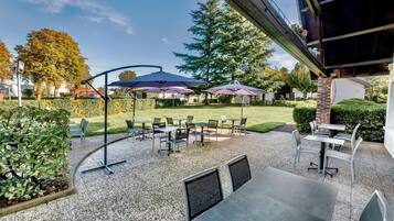 Un patio al aire libre con mesas y sillas, rodeado de follaje y árboles.