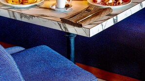Een ontbijtsetting met een marmeren tafel, een blauwe bekleden bank, croissants, ham, eieren en sinaasappelsap.