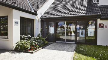 A building with a tiled roof, a glass entrance, and a small garden area with plants.