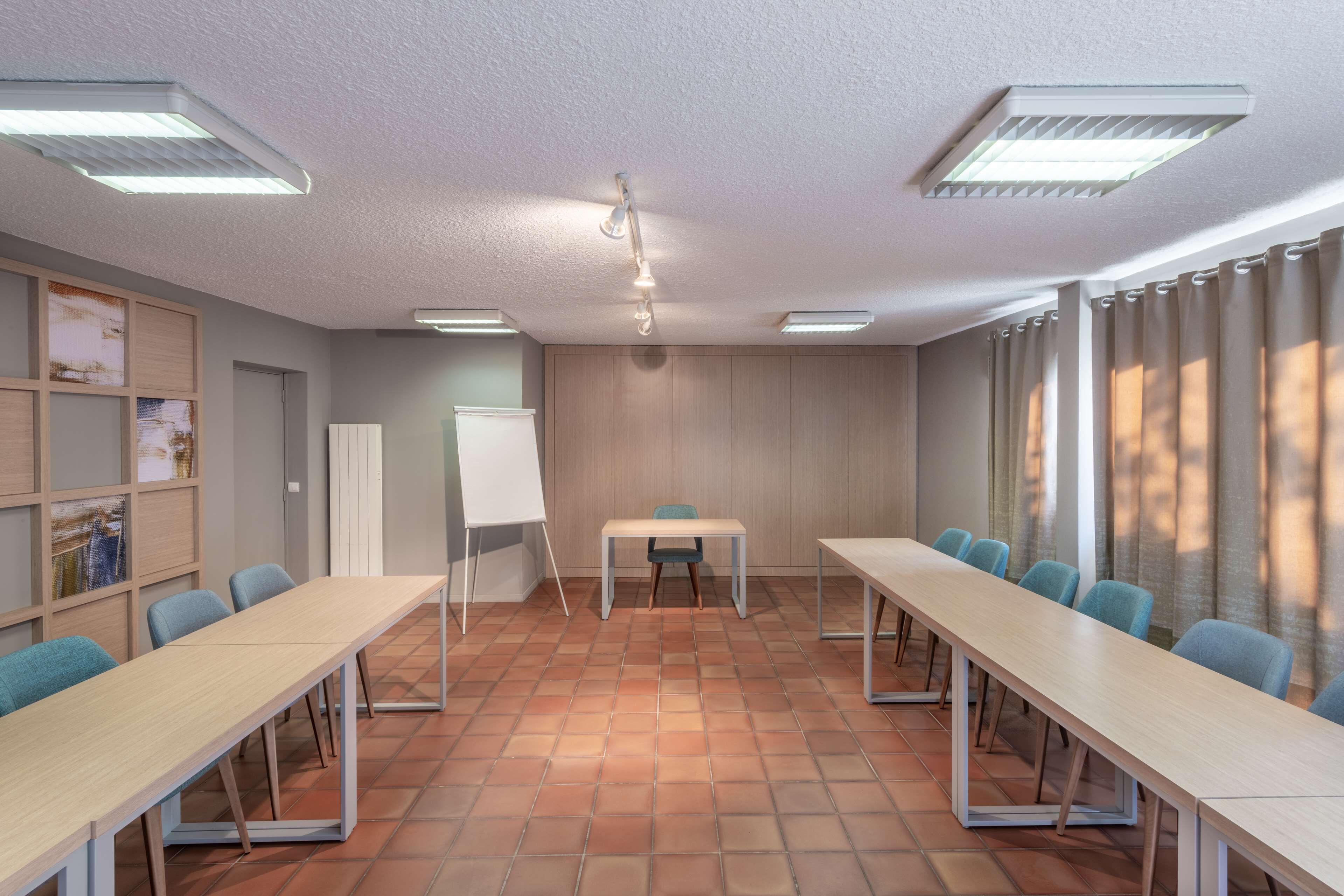 Uma sala de conferências com mesas compridas, cadeiras, um quadro branco e um projetor.