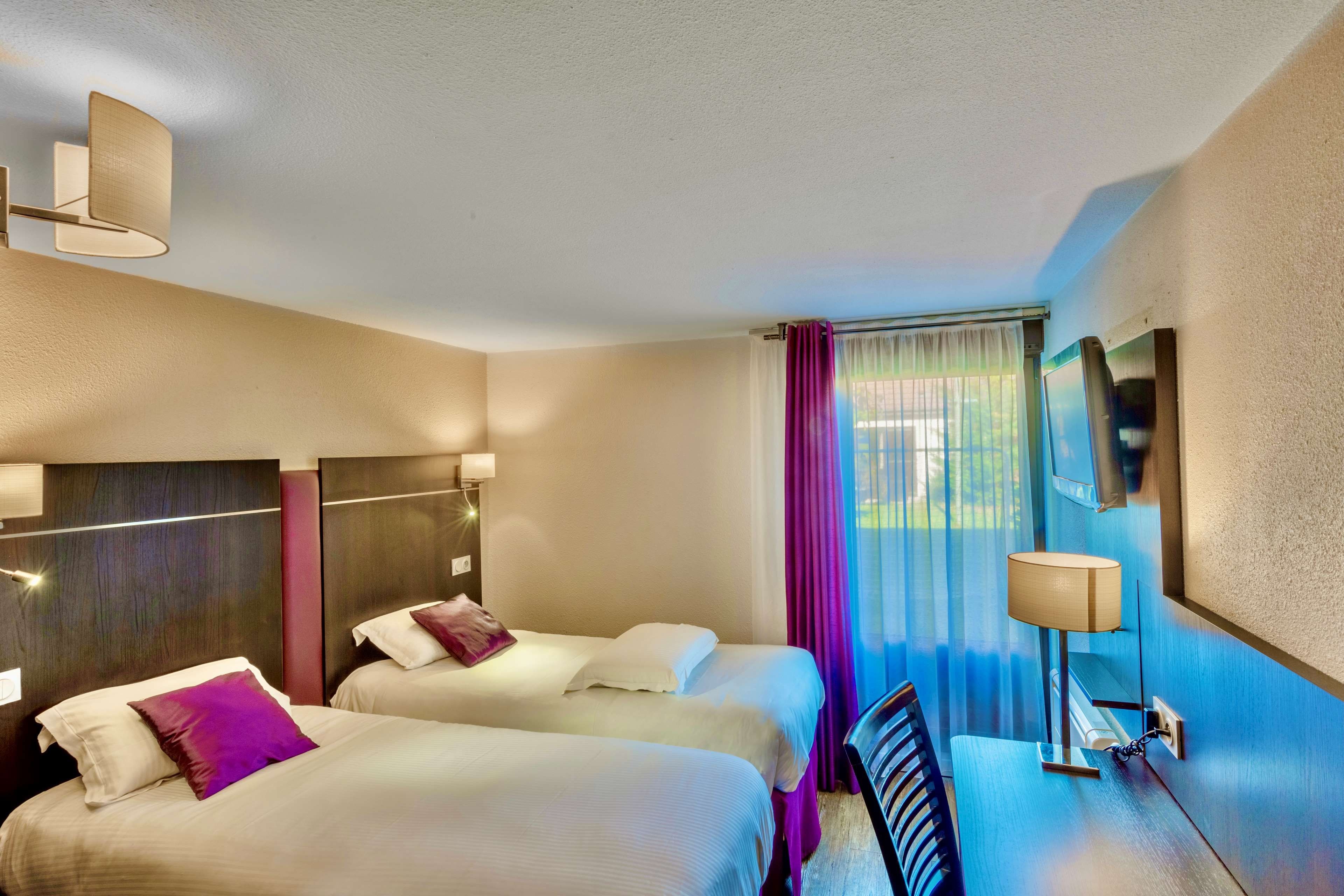 A hotel room with two beds, a desk, a chair, a TV, and a window with curtains.